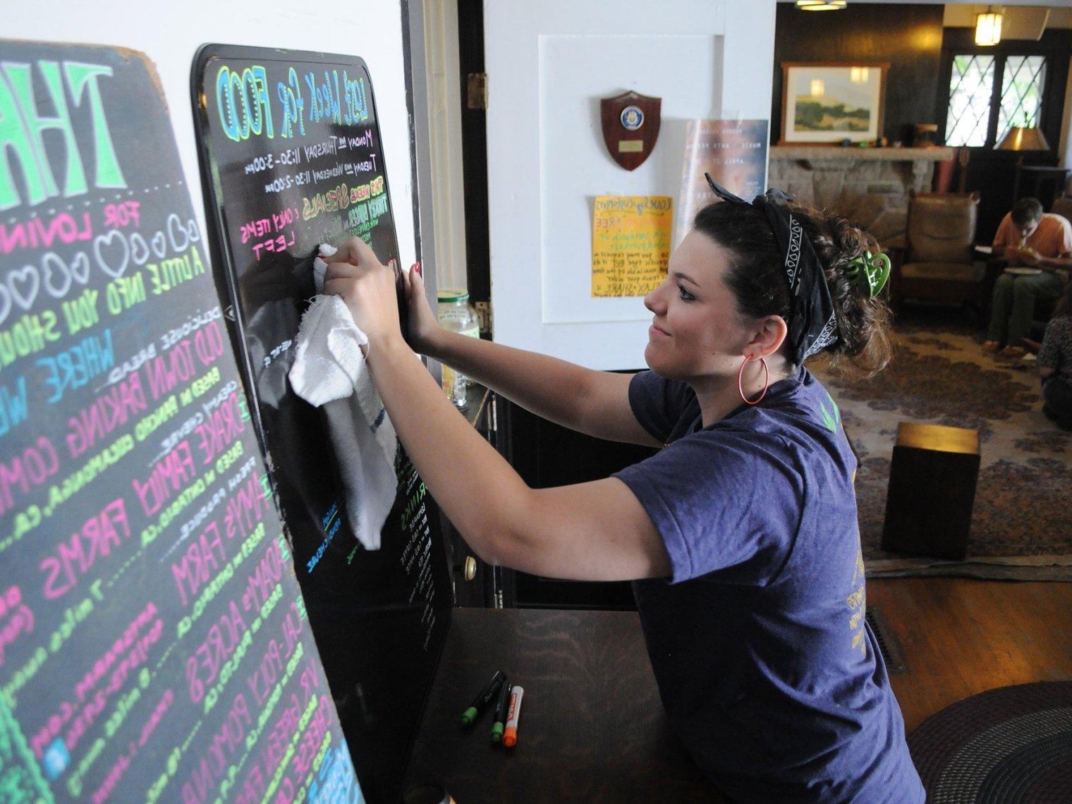 a student grove house kitchen worker updates the chalk menu